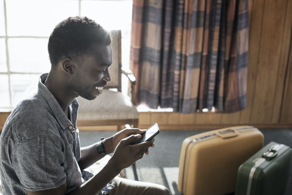 A young man in a motel room checking his smart phone.