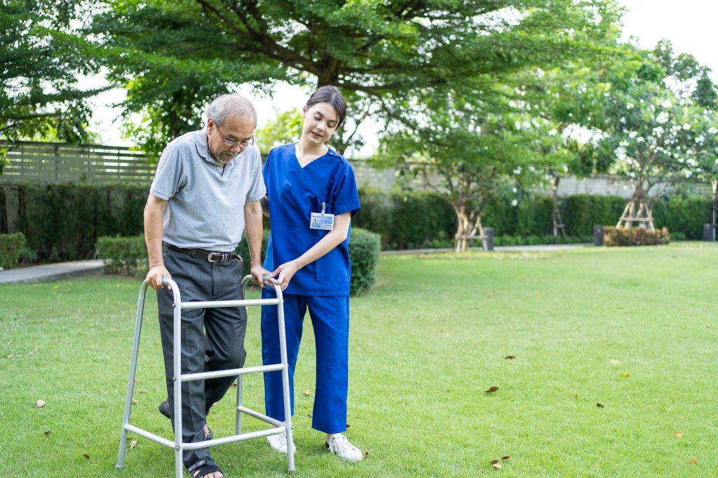 Asian young woman nurse at nursing home take care disabled senior man at backyard.