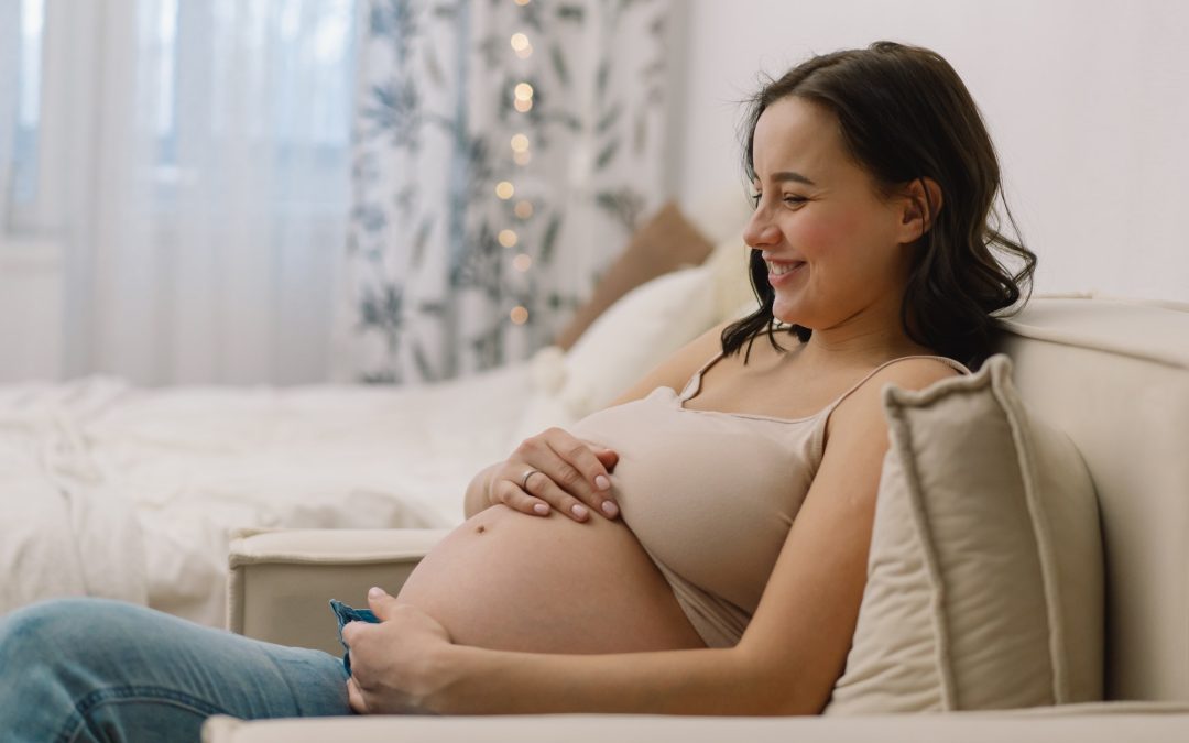Attractive pregnant woman is sitting in armchair and holding her belly. Last months of pregnancy.