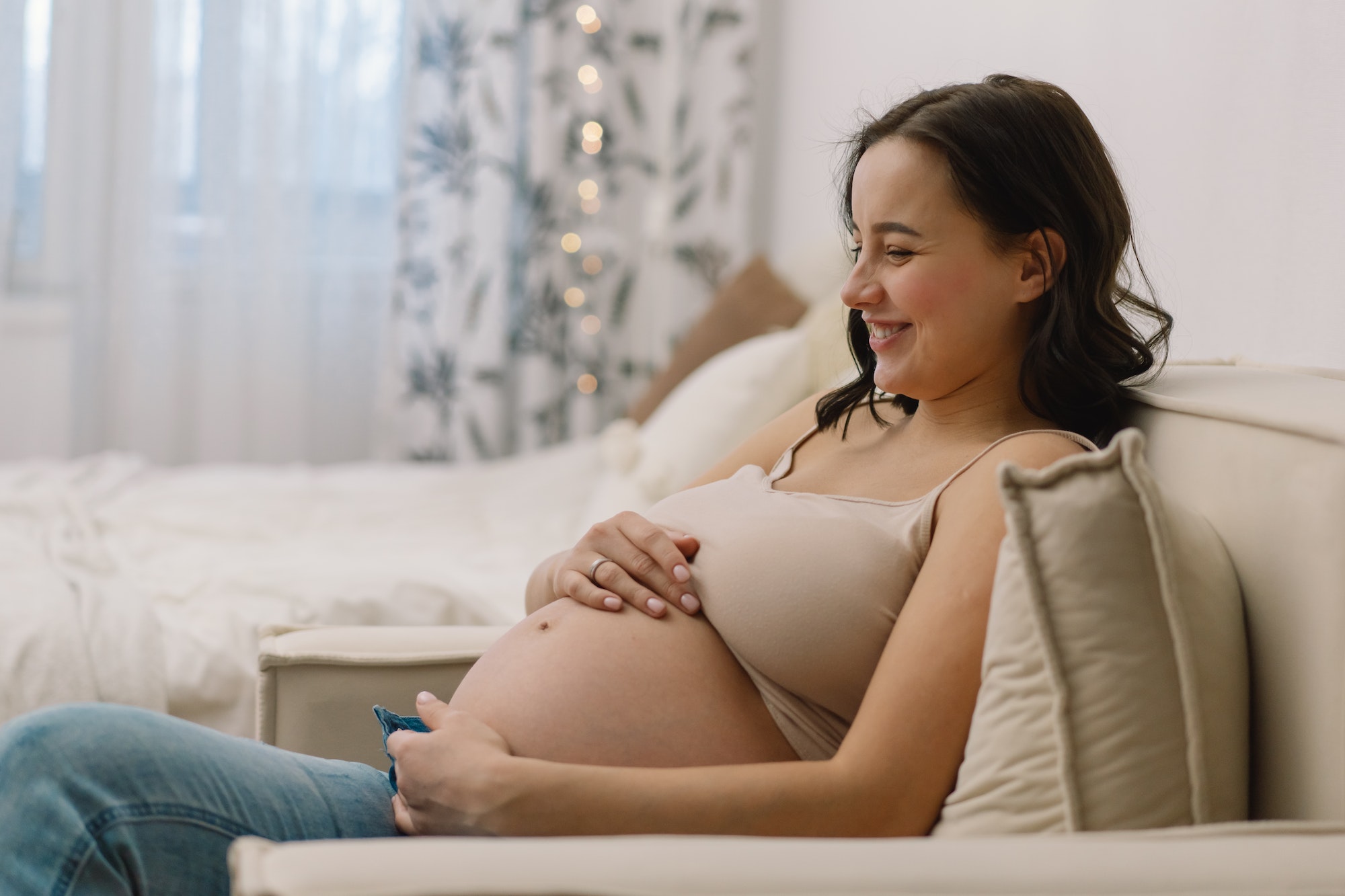 Attractive pregnant woman is sitting in armchair and holding her belly. Last months of pregnancy.