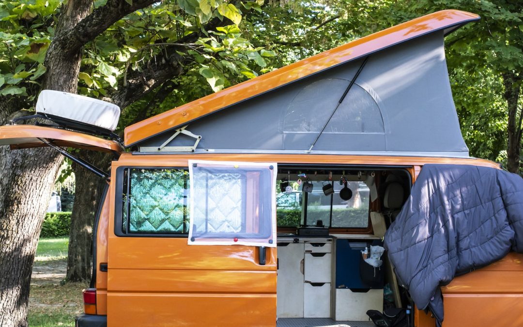 Camper in campsite. Outdoor equipment and travel van on green me