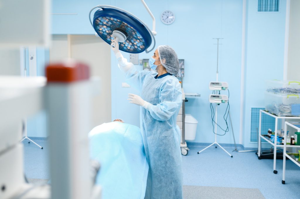 Female surgeon prepares lamp in operating room