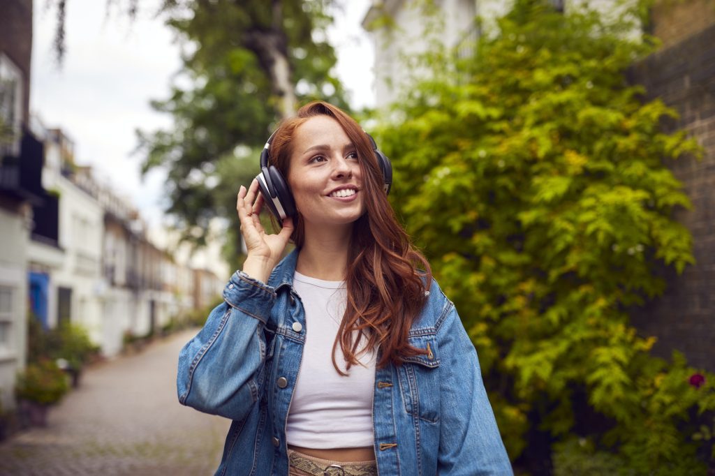 Female Vlogger Or Social Influencer Wearing Headphones Travelling Through City