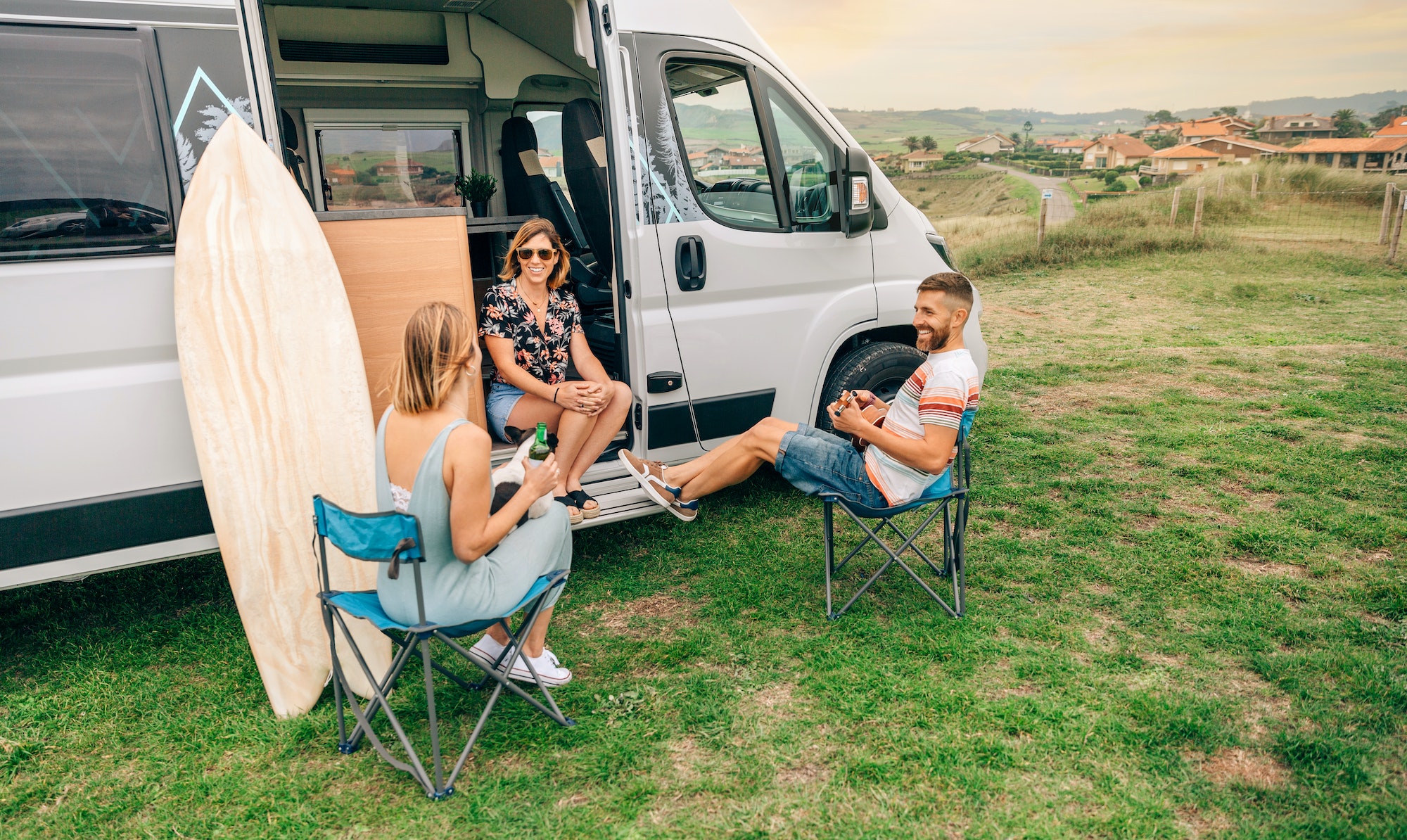 Friends with their dog talking and drinking beer in front of their camper van