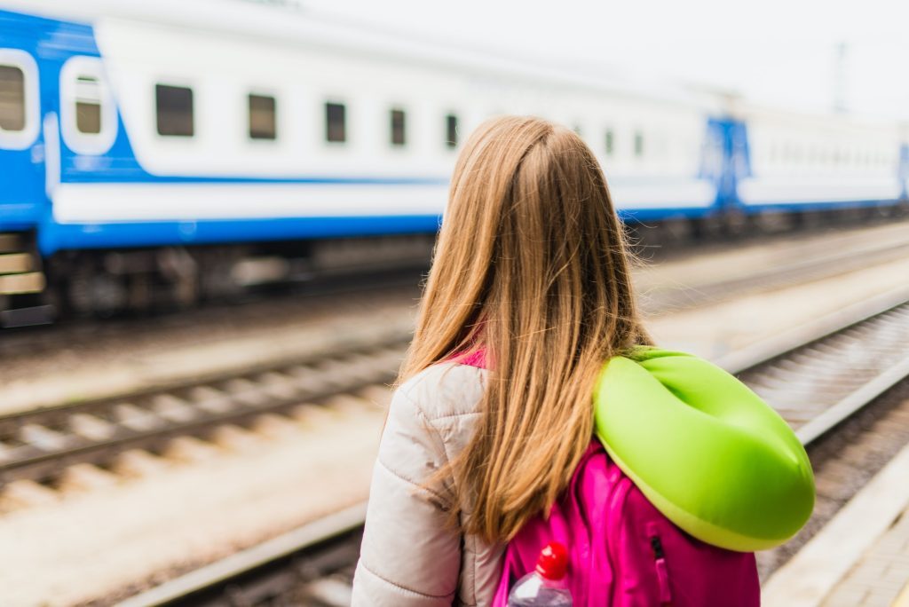 Girl is waiting for the train. Girl with a backpack and with green neck pillow