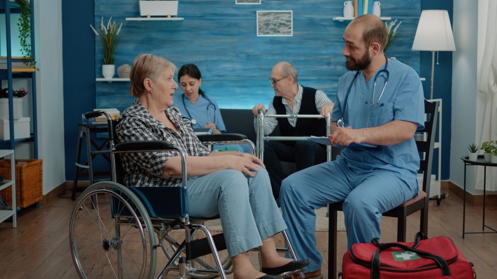 Man nurse consulting elder woman with disability in nursing home