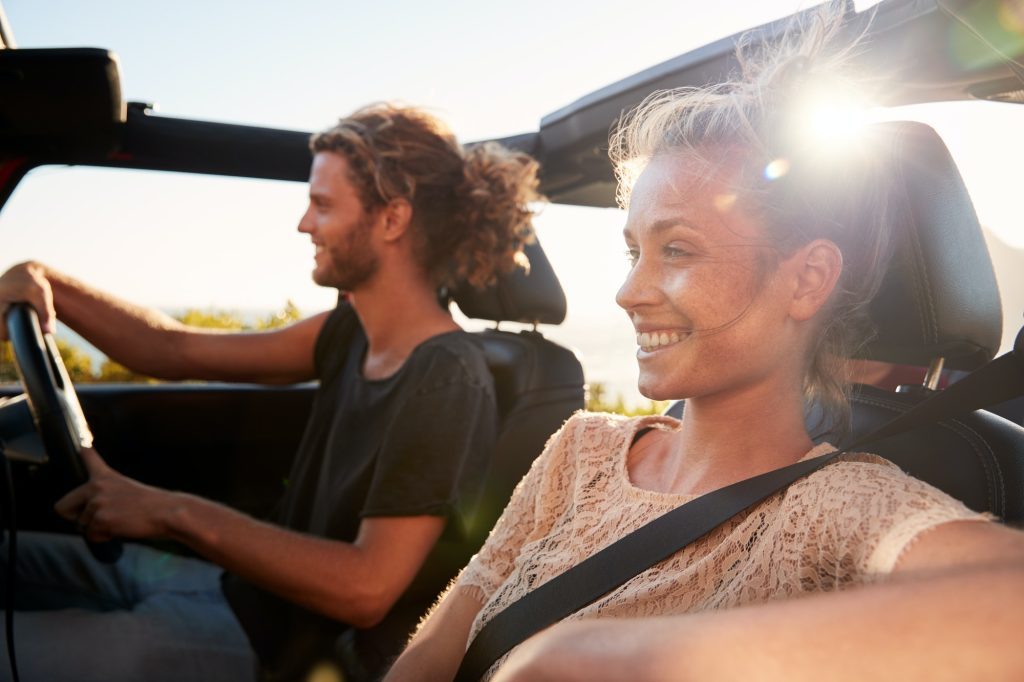 millennial-white-couple-on-a-road-trip-driving-in-an-open-top-car-backlit-close-up-1024x682-4467348