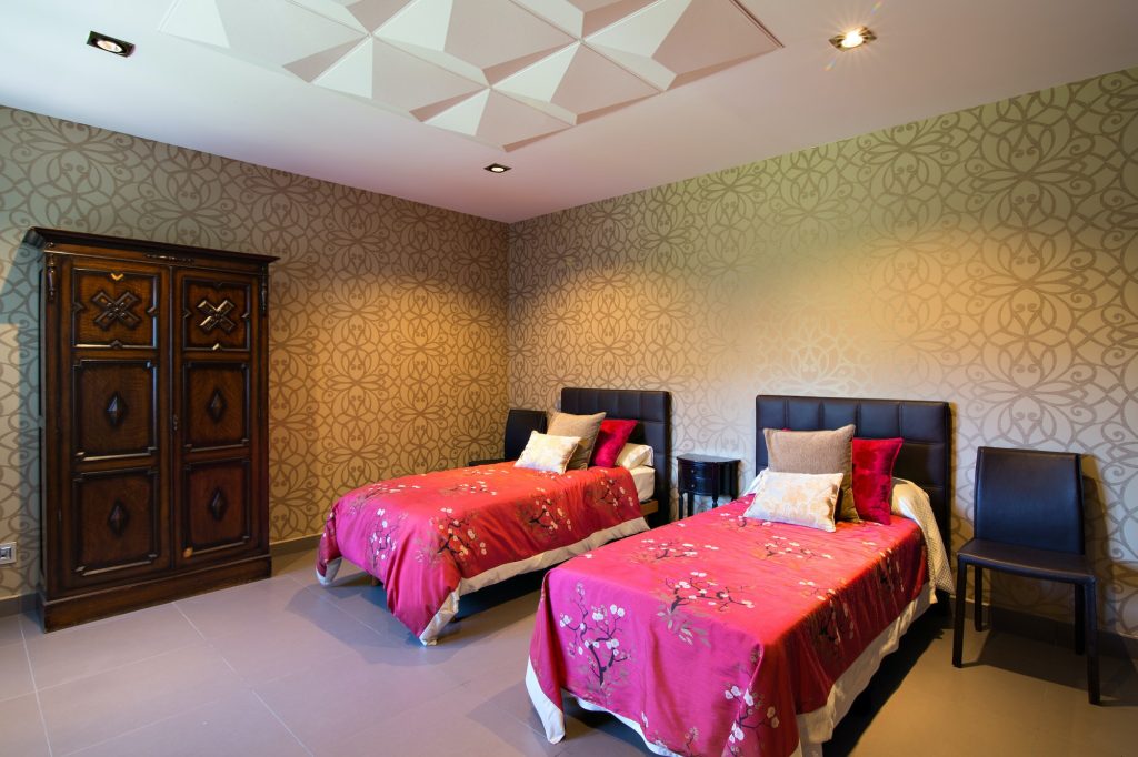 Modern house room, with wallpaper and two single beds with fuchsia duvets. Decorative ceiling.