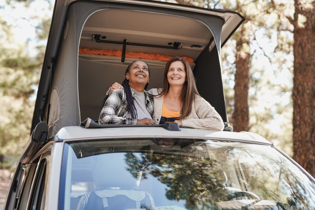 Multiracial women enjoy road trip vacation with mini van camper and looking out on roof top