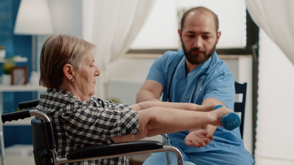 Nurse assisting disabled patient with physical exercises for recovery