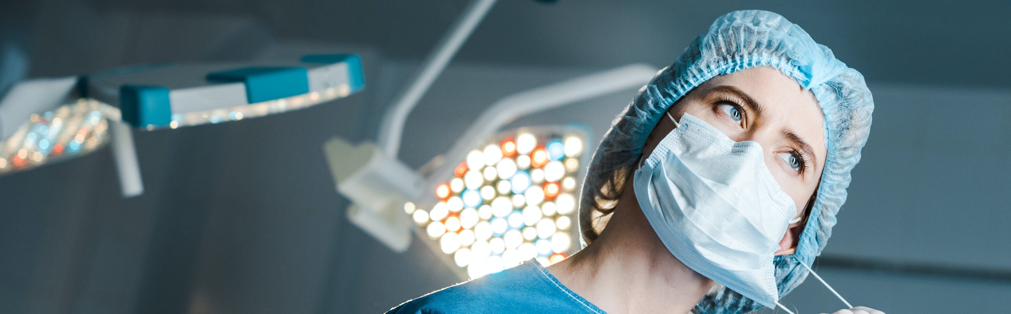 panoramic shot of nurse putting off medical mask in operating room
