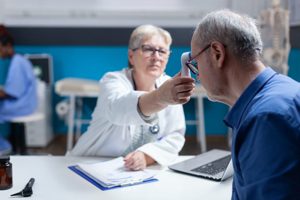 Physician using thermometer to measure temperature of aged patient
