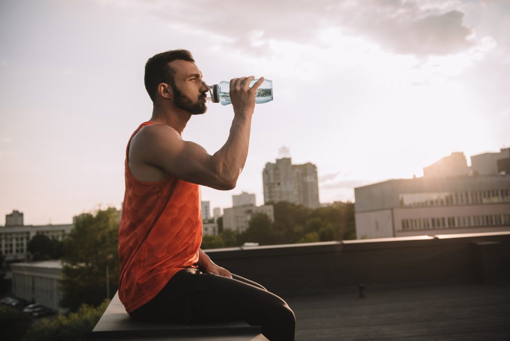 side view of handsome sportsman drinking water from sport bottle on roof