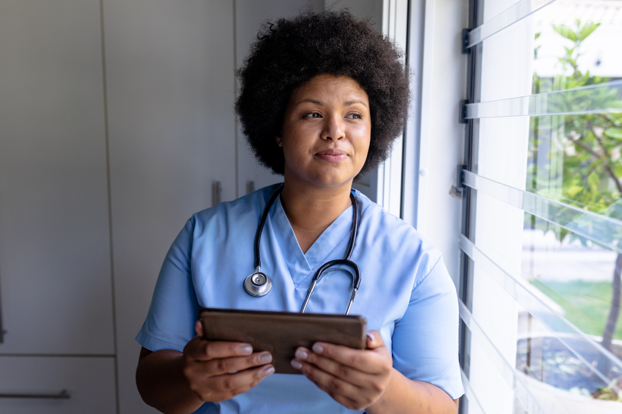 Smiling african american mid adult female nurse looking away while holding digital tablet