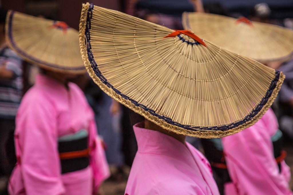 Three woman in big woven hats performing japanese folk dance