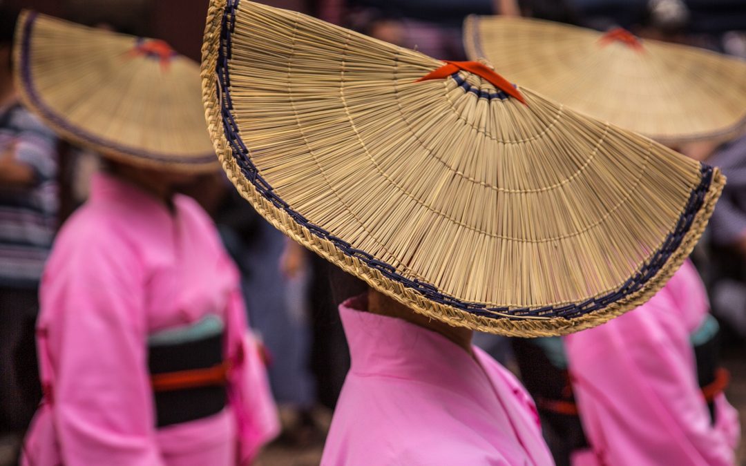 Three woman in big woven hats performing japanese folk dance