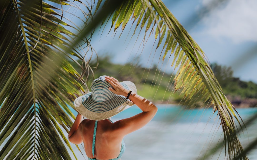 Woman on the beach in the palm trees shadow wearing blue hat. Luxury paradise recreation vacation
