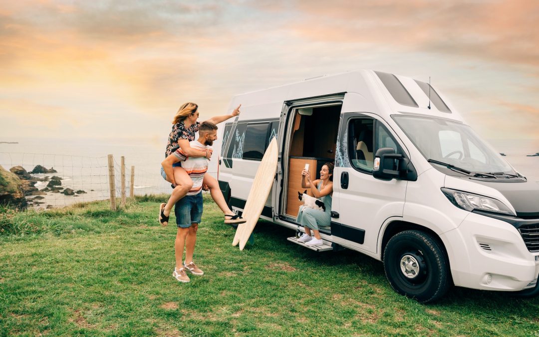 Woman taking photo with mobile of her friends piggybacking next to their camper van during a trip