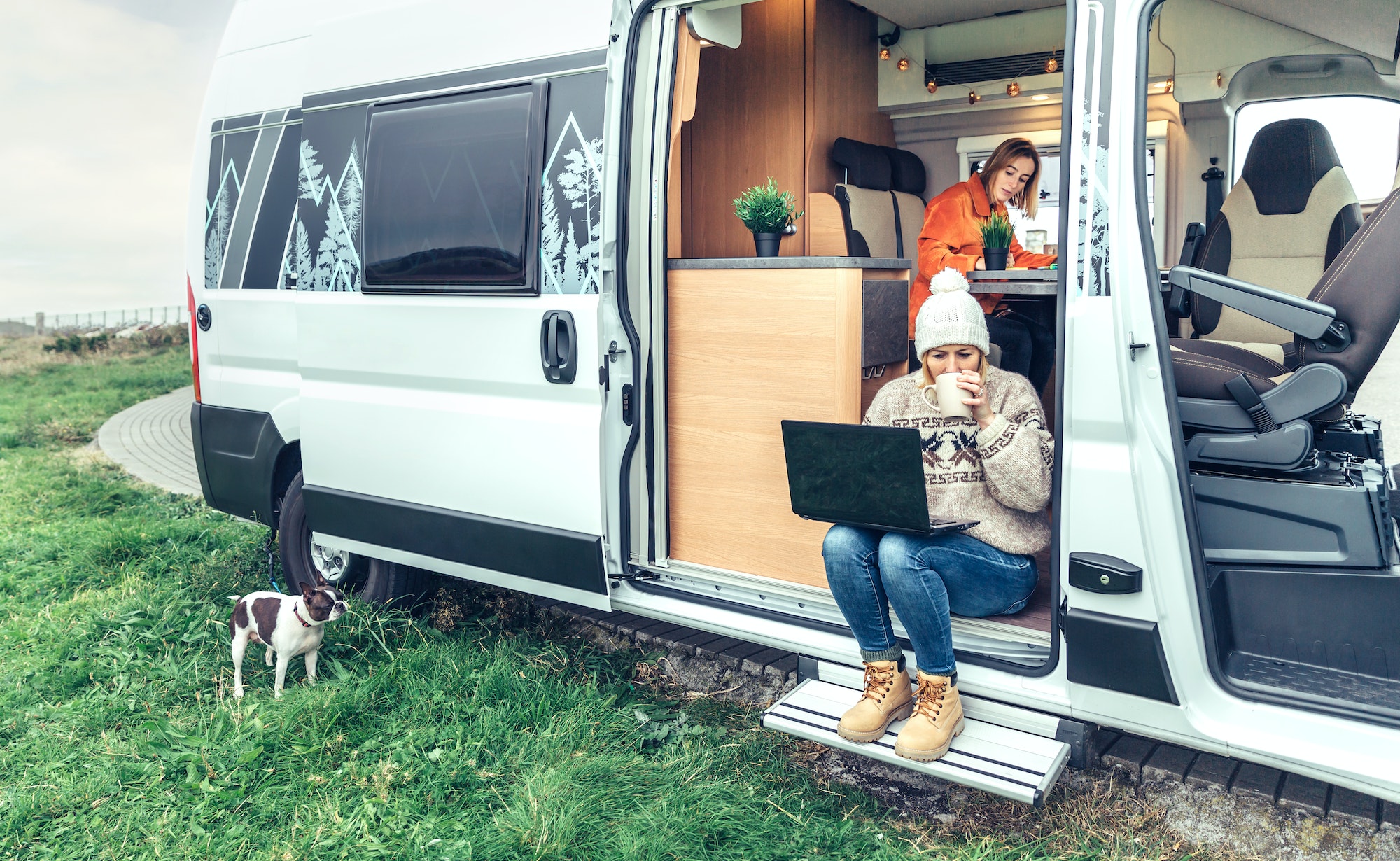 Woman teleworking drinking coffee sitting in the door of a camper van