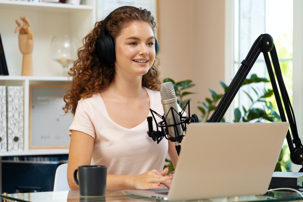 Woman vlogger looking at laptop and recording video with microphone