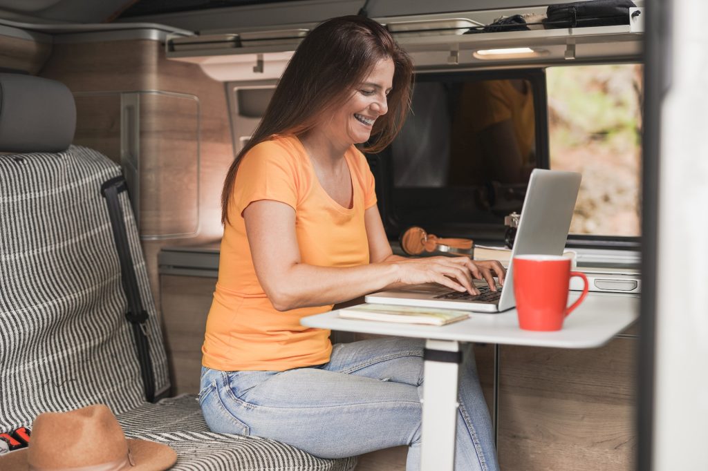 Woman working inside mini van camper using computer laptop