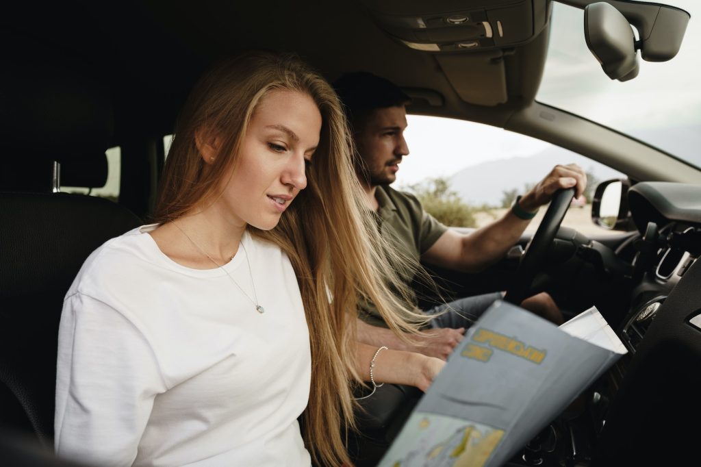 Young loving couple on a road trip using map inside a car