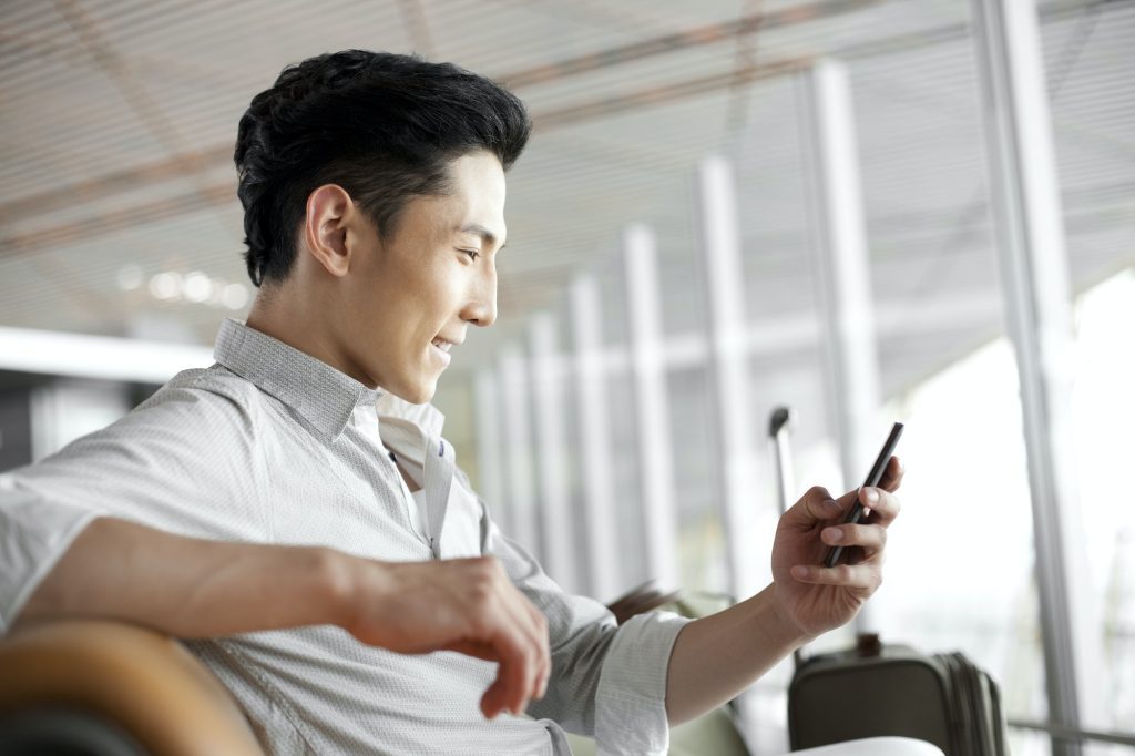 Young man with smart phone waiting in airport lounge